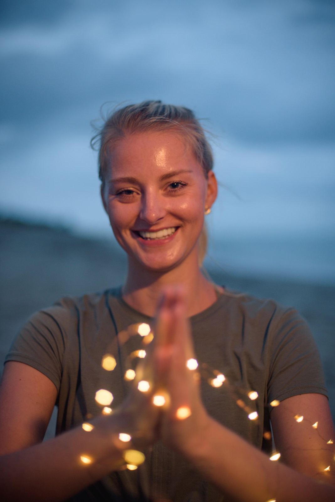 Corey Heyman smiling with her hands in prayer on the beach