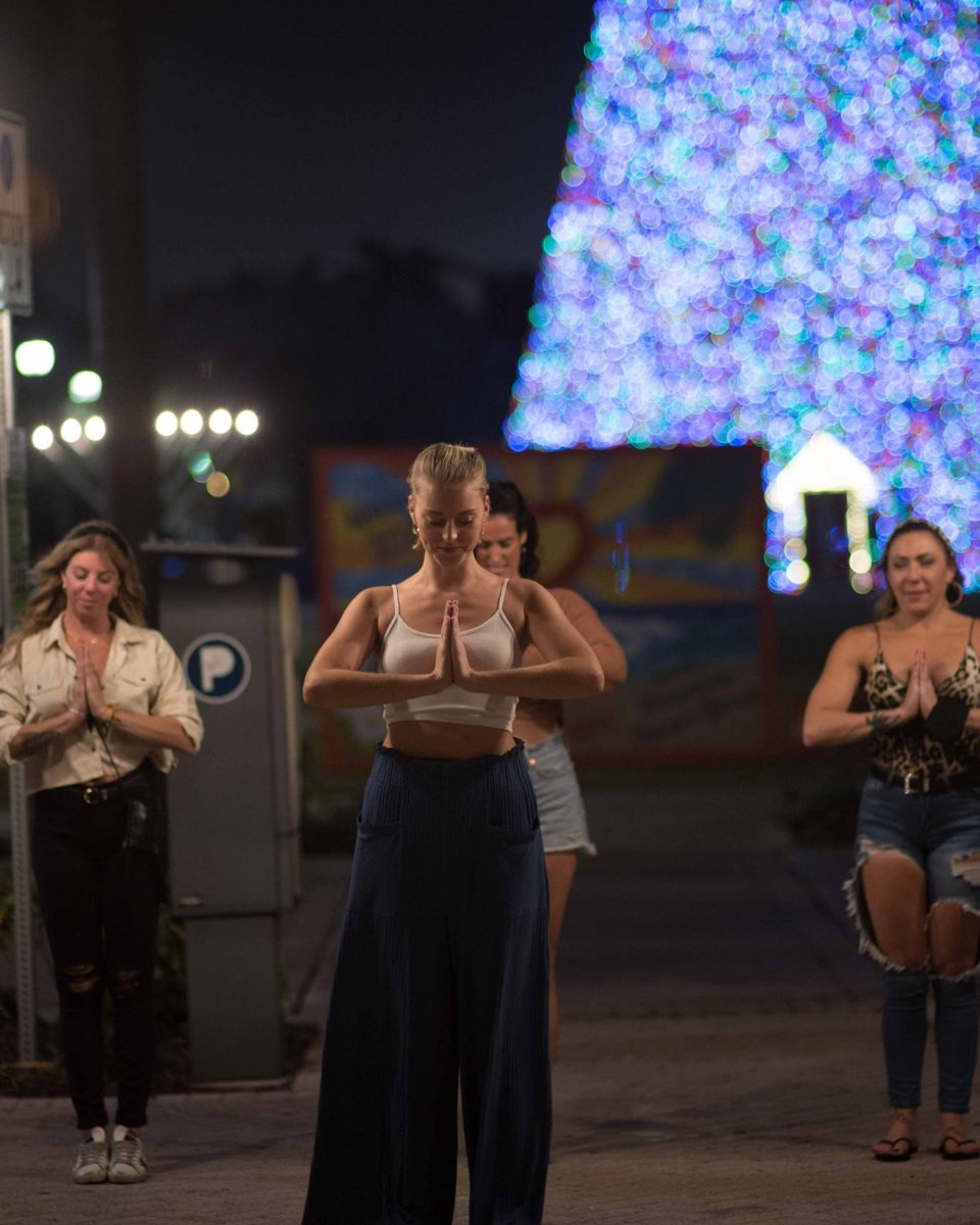 Corey leading a group of women in prayer pose in front of holiday lights at night